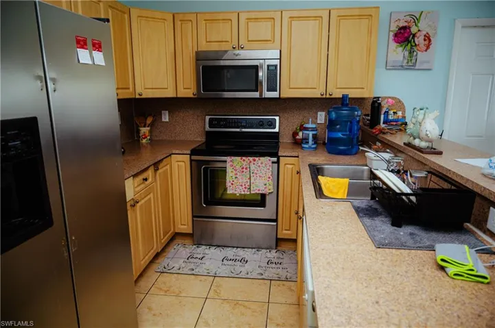 Kitchen featuring light wood cabinetry, stainless steel appliances, speckled countertops, a double basin sink, and tile flooring