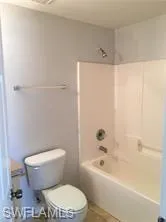 Bathroom featuring a white toilet, white bathtub with a shower, and light-toned wall paint