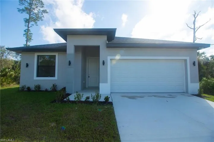 Single-story exterior featuring a stucco facade, covered entryway, two-car garage, concrete driveway, and wall-mounted exterior lighting fixtures
