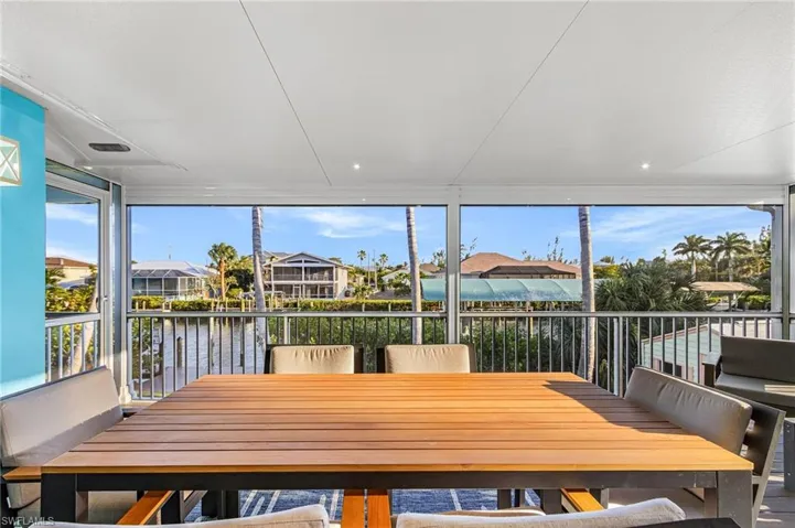 Screened lanai featuring a wood-slat dining table and direct waterfront access
