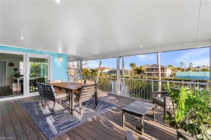 Screened outdoor living space featuring composite decking, recessed lighting, a sliding glass door, and water views with tropical foliage