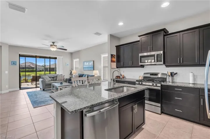 Kitchen with decorative backsplash, an island with sink, stainless steel appliances, ceiling fan, and sink