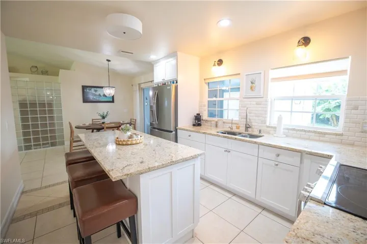 Kitchen with light tile patterned floors, lofted ceiling, a center island, stainless steel refrigerator with ice dispenser, and white cabinetry
