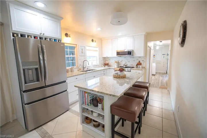 Kitchen featuring stainless steel appliances, light tile patterned flooring, white cabinets, a breakfast bar area, and recessed lighting