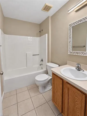 Bathroom featuring a full tub and shower combination, a single vanity with wood-finish cabinetry, a large mirror with a mosaic-tiled frame, and neutral tiled flooring