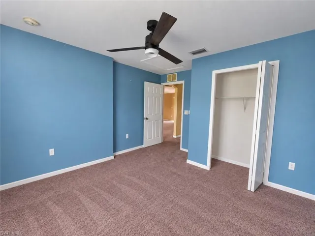 Ceiling fan with dark wood-finish blades, soft carpet flooring, built-in closet with bi-fold doors, and a white interior door