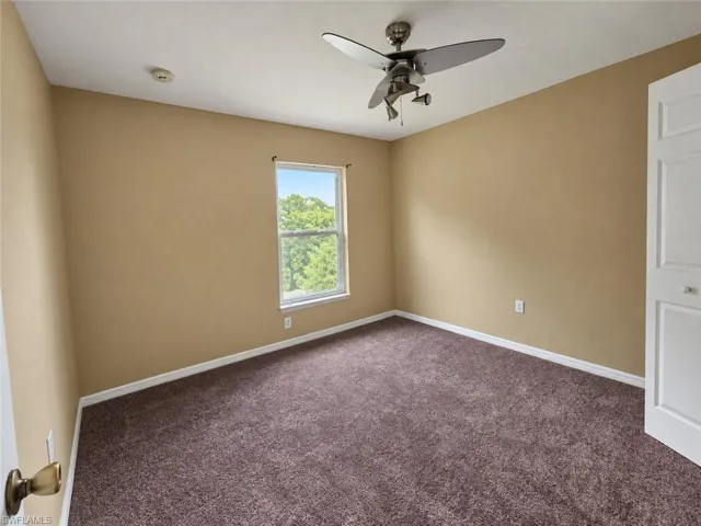 Neutral wall paint, brown carpet flooring, single window, ceiling fan with integrated lighting, and a paneled door