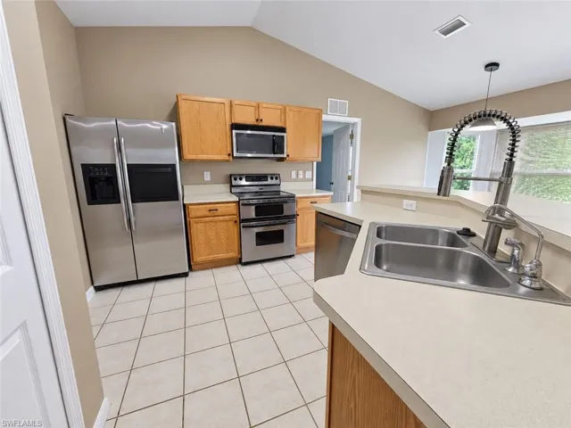 Kitchen featuring a vaulted ceiling, stainless steel appliances, wood-finish cabinetry, a double basin sink, and tile flooring