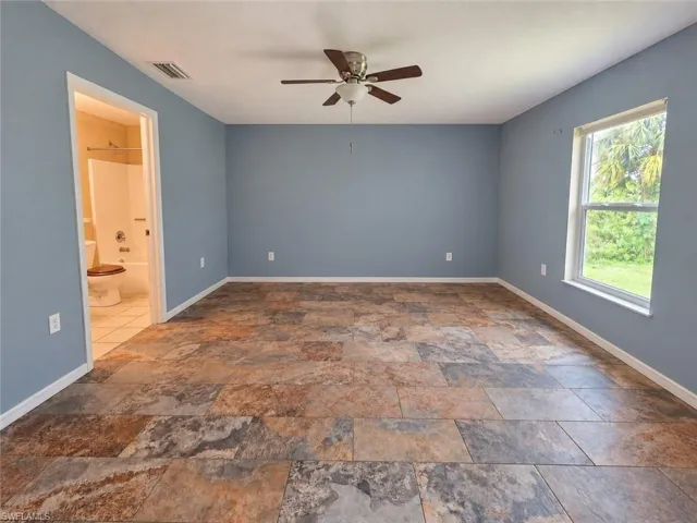 Spacious room featuring multi-toned tile flooring, light blue walls, and a ceiling fan