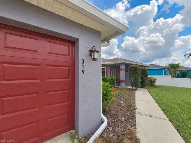 Panel-style garage door, exterior wall lantern, concrete walkway, landscaped front yard, and stucco exterior finish