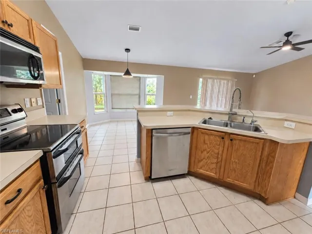 Kitchen featuring stainless steel appliances, wood cabinetry, tile flooring, and a ceiling fan