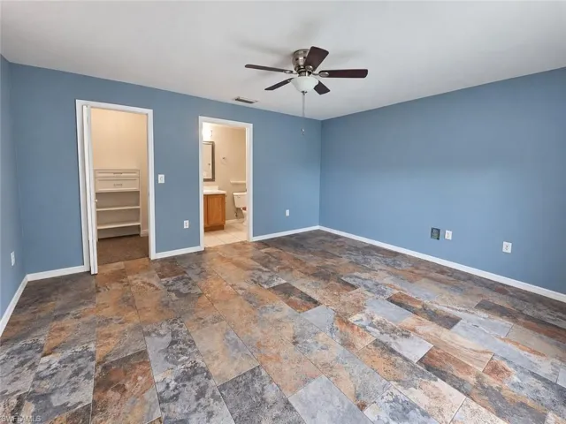 Spacious room featuring slate-look flooring, ceiling fan with integrated lighting, and direct access to a closet with built-in shelving