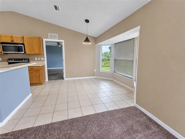 Vaulted ceiling, modern pendant lighting, tiled flooring, bay window, light wood-finish cabinetry
