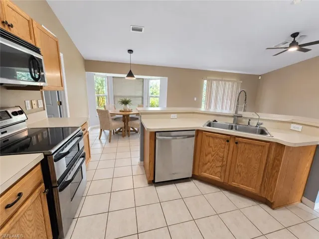 Kitchen featuring light wood cabinetry, white tile flooring, stainless steel appliances, a double basin sink, and a ceiling fan