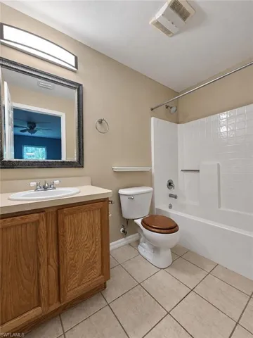 Bathroom with a wood-finish vanity, light-toned countertop, integrated sink, tile flooring, and a shower-tub combination with white subway tile surround