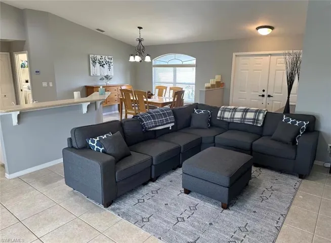 Living room with light tile patterned flooring, suspended lighting, and lofted ceiling
