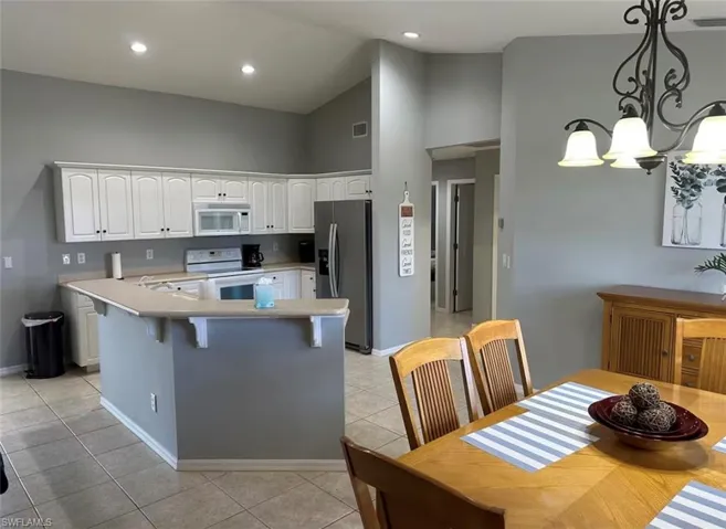 Kitchen featuring vaulted ceiling, white cabinetry, white appliances, light countertops, and a breakfast bar