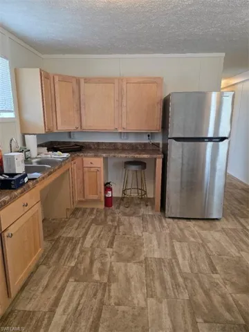 Kitchen with fridge, light brown cabinetry, a textured ceiling, a breakfast bar, and crown molding