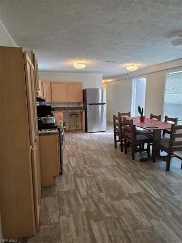 Kitchen featuring stove, stainless steel fridge, light brown cabinets, dark countertops, and a textured ceiling