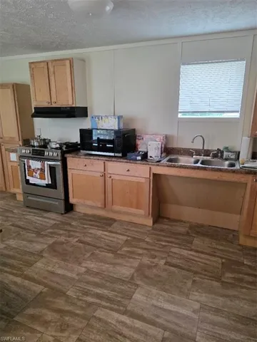 Kitchen with stove, a textured ceiling, white microwave, dark countertops, and exhaust hood