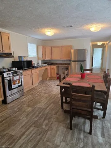 Kitchen featuring dark countertops, range, fridge, a textured ceiling, and light brown cabinets