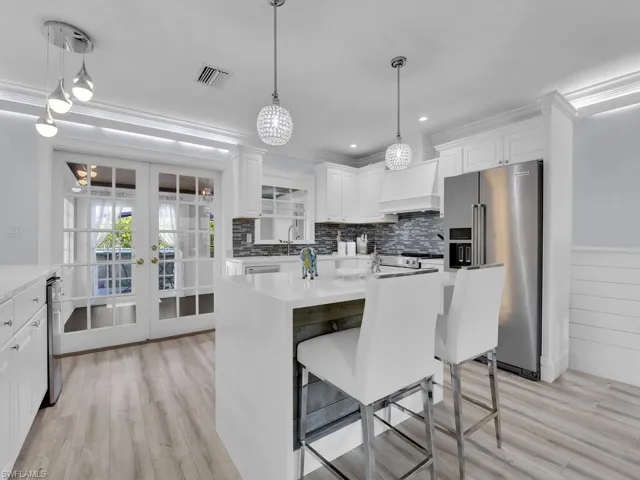 Kitchen featuring white cabinets, light vinyl wood-style flooring, high quality fridge, and premium range hood