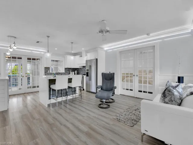 Living room with light vinyl wood-style floors, french door to master bedroom, ornamental molding, and ceiling fan