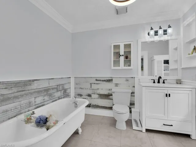 Bathroom featuring tile flooring, ornamental molding, shiplap accents, vanity, traditional clawffot tub and toilet
