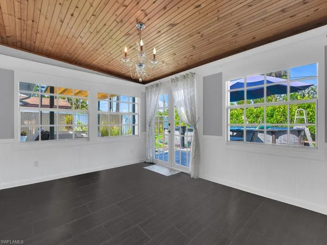 Bonus room soibles as sunroom or private dining area with an inviting chandelier, wide-plank tiles, french doors to patio, and wooden ceiling