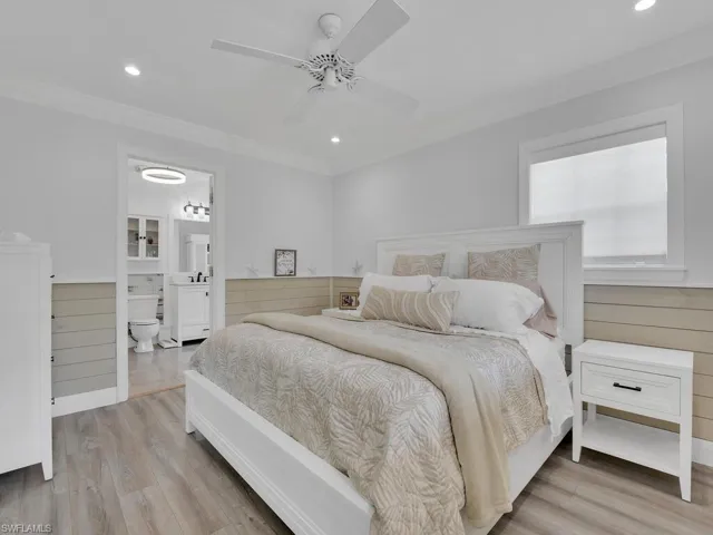 Master bedroom with ceiling fan, light vinyl wood-style floors, crown molding, shiplap accent walls and connected bathroom