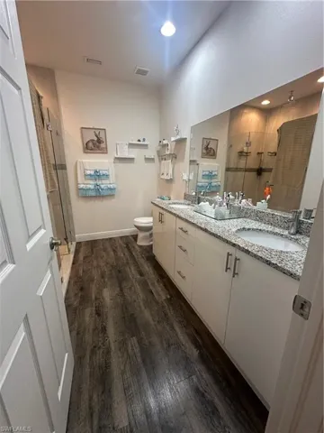 Full bathroom with dark wood-style floors, a stall shower, and double vanity
