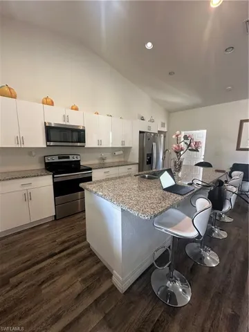 Kitchen with white cabinets, range, lofted ceiling, refrigerator, and light stone counters
