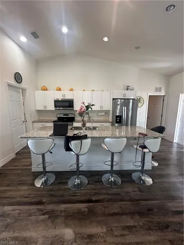Kitchen featuring a kitchen breakfast bar, white cabinets, lofted ceiling, white appliances, and a spacious island
