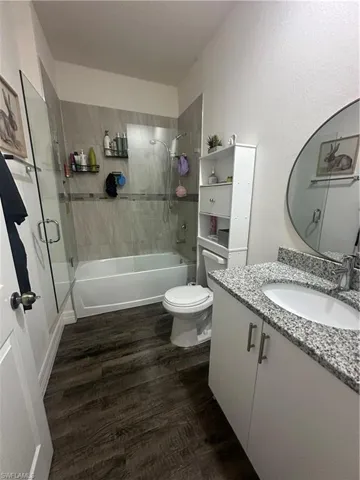 Bathroom with vanity, dark wood finished floors, and combined bath / shower with glass door