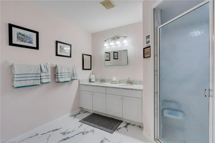 Full bathroom featuring a stall shower, double vanity, and light marble finish flooring