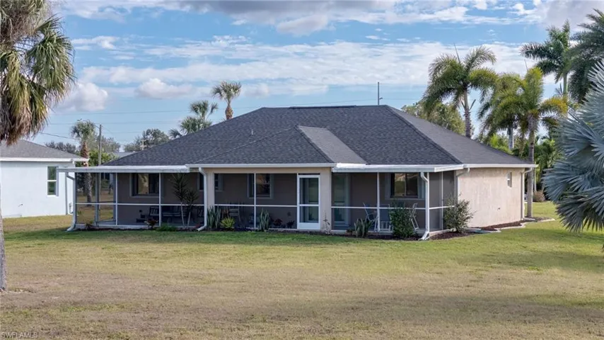 Rear view of house with a yard, a sunroom, stucco siding, and roof with shingles