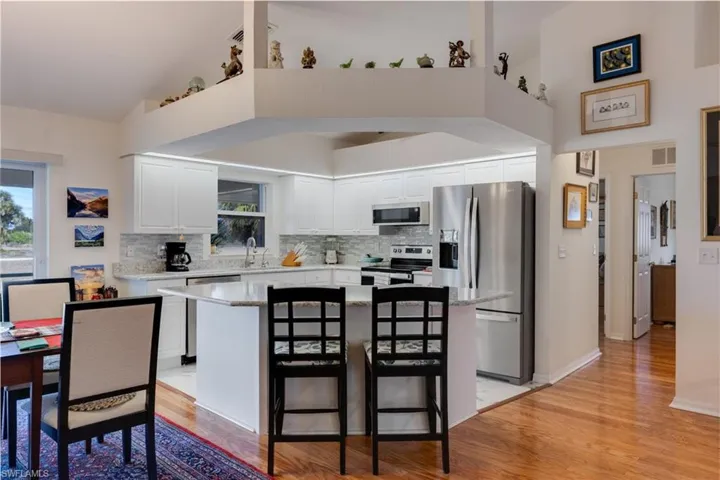 Kitchen with appliances with stainless steel finishes, white cabinetry, light wood-style flooring, a center island, and a towering ceiling