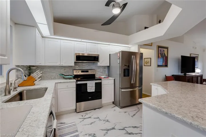Kitchen with appliances with stainless steel finishes, white cabinetry, light marble finish floors, lofted ceiling, and decorative backsplash