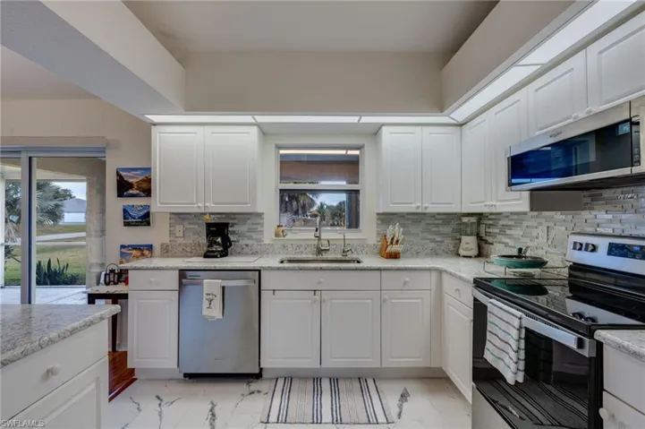 Kitchen with stainless steel appliances, white cabinets, light marble finish floors, tasteful backsplash, and light stone counters