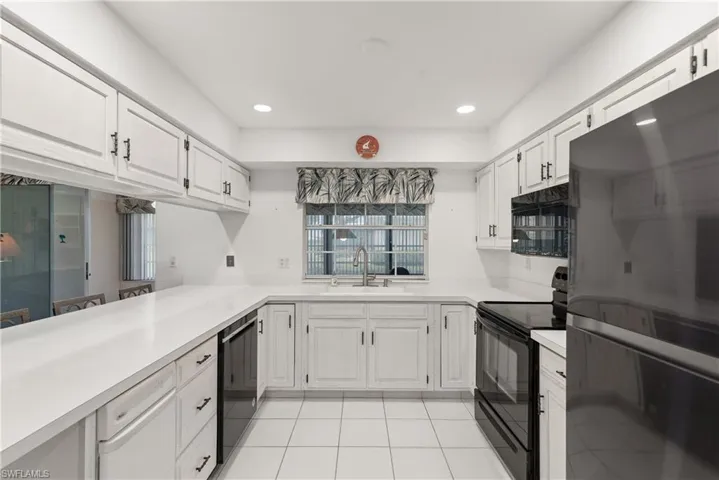 Kitchen featuring black appliances, a sink, light countertops, light tile patterned floors, and white cabinets