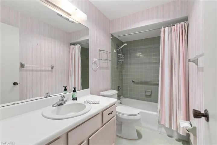 Bathroom featuring wallpapered walls, vanity, toilet, shower / bath combo with shower curtain, and tile patterned flooring