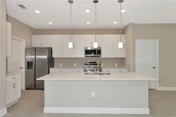 Kitchen featuring white cabinetry, decorative light fixtures, tasteful backsplash, appliances with stainless steel finishes, and a kitchen island with sink