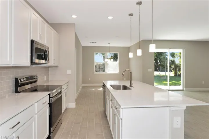 Kitchen with white cabinetry, stainless steel appliances, sink, decorative backsplash, and a center island with sink