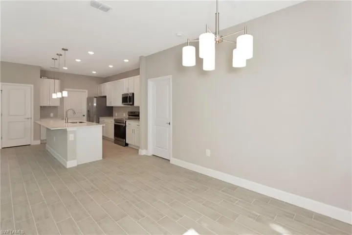 Kitchen with stainless steel appliances, white cabinets, decorative light fixtures, backsplash, and a kitchen island with sink
