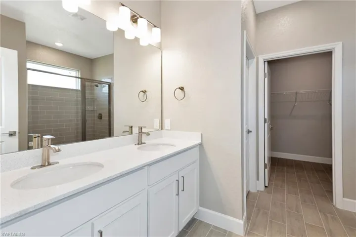 Bathroom with a shower with shower door, double sink vanity, and tile patterned flooring