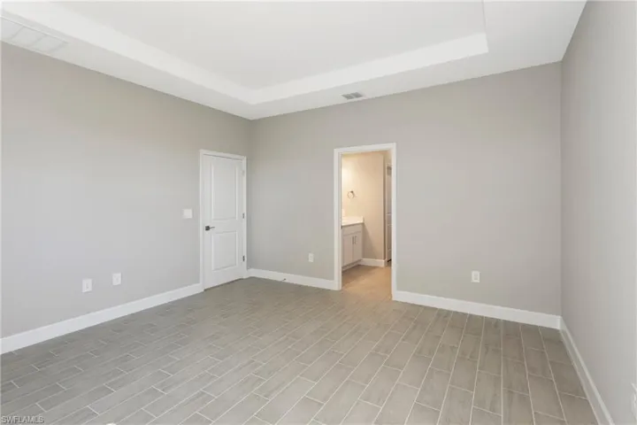 Unfurnished bedroom featuring light hardwood / wood-style floors, a raised ceiling, and ensuite bathroom