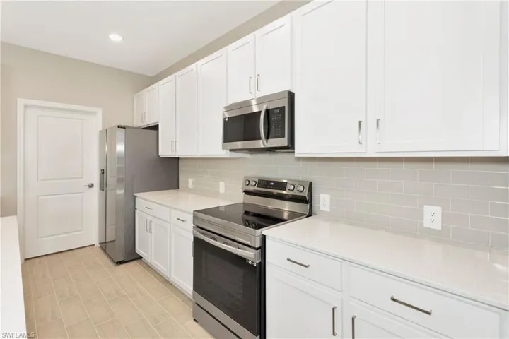 Kitchen with light tile patterned floors, white cabinets, backsplash, and stainless steel appliances