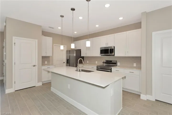 Kitchen featuring stainless steel appliances, white cabinets, sink, backsplash, and an island with sink