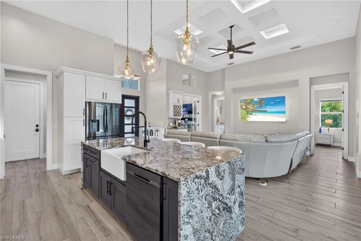 Kitchen island featuring a farmhouse sink, stone countertops, and pendant lighting