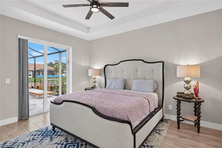 Tray ceiling with a ceiling fan, sliding glass door, and wood-finish flooring